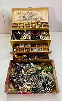 Three-tier jewelry box filled with assorted bracelets, necklaces and beads on top, middle drawers with loose earrings and rings, loose box at bottom