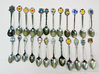 Photo showing full collection of 20 silver plated souvenir spoons arranged in two rows with colorful enamel crests on each handle top.