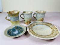 Photo of three JP Star pottery mugs and two dishes, showing shapes and glaze colors.