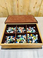 Top view of the open hideaway book storage box showing six compartments filled with multicolored vintage marbles.