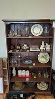 Front view of the cabinet showing four adjustable shelves with various glassware and decorative items (not included in sale).