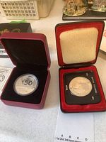 Two silver dollar coins in their original cases; left is Canada 150th anniversary coin, right is British Columbia centennial coin.