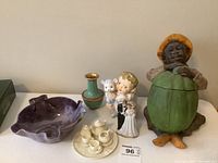 Photo showing all items: miniature tea set, bride and groom figurine, green vase, purple leaf bowl, and lidded figure of boy with green pod