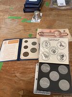 Calgary Stampede souvenir dollars display with six silver coins and an insert showing obverses alongside a Canadian 2 dollar bill on a wooden surface.