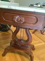 Front view of the mahogany table showing the dovetailed drawer with carved floral handle and the marble top.