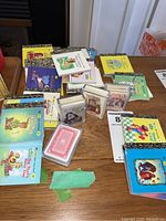 Photo showing an assortment of miniature Little Golden Books with multiple decks of playing cards arranged on a table, showcasing the quantity and variety.