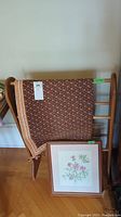 Quilt rack holding the patterned quilt with framed print on floor