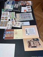 Overview of stamp sheets and albums laid out on black table, showing multiple Canadian commemorative themes and the New Zealand stamp.