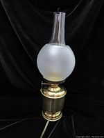Brass oil lamp shaped table lamp with frosted globe and glass chimney from front on black background