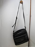 Full view of black leather crossbody handbag hanging showing overall condition and design