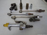 Close view of 9 metal air tool components including one chrome air blow gun with yellow tip, various metal fittings, adapters, and connectors.