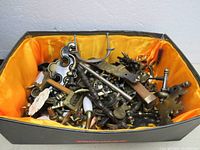 Box filled with assorted vintage cabinet drawer puller knobs and back plates on orange lining, showing variety of metal parts with some porcelain handles and visible wear.