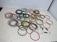 Overview of variety of 72 bracelets including metal bangles, plastic bangles, and bead bracelets arranged on white surface.