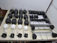 Top-down view of various black and white plastic caster wheels arranged in rows including metal wheel frames.