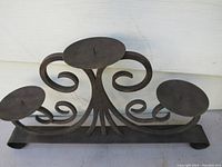 Front angle of the metal candle holder showing three round candle platforms and decorative curved metalwork with a flat base.