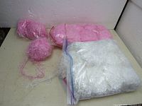 Lot showing pink fuzzy yarn skeins and white fuzzy yarn in a clear plastic bag on a beige surface against a white wall.