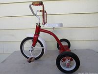 Side view of red Radio Flyer toddler tricycle showing white seat, handlebars with red tassels, and 10 inch wheels with black hard rubber tires.
