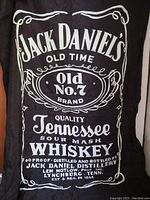 Front view of the black polyester Jack Daniels Old No. 7 banner flag with white print and some wrinkles.