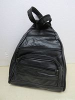 Front view of a black leather purse designed like a backpack, showing multiple zippered compartments.