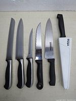 Set of six black handled knives laid flat showing different blade styles and lengths with one Wiltshire knife in white sheath sharpener.