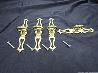 Four vintage brass drawer pullers laid out on dark fabric with their original screws, showing overall shape and finish.
