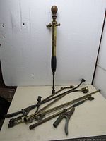 Full view of vintage brass garden sprayer with multiple brass attachments and small hand tool on white surface