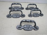 Lot of five vintage metal cabinet drawer pullers arranged on a flat surface