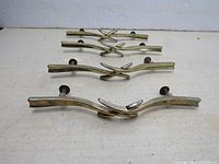 Four vintage brass cabinet drawer pullers laid out in a row on a white surface showing their curved crossed design and attached screws.