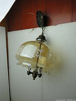 Side angle view of vintage ceiling light hanging on chain with amber glass shade and floral white flower pattern
