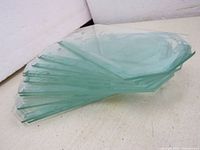 Stack of 12 clear beveled and etched octagon glass chandelier/lamp panels with a light green tint, edges visible, stacked on a white surface.