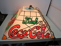 Side view of square swag lamp shade showing 'Drink Coca Cola' text in red with black outline, black grid lines, and part of metal hanging chain.