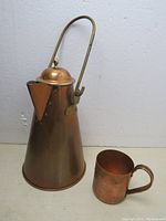 Front angle view of vintage tall copper coffee pot swing handle and copper Moscow mule mug on white surface.