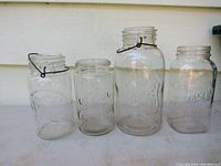 Four vintage clear glass canning jars arranged side-by-side showing different sizes and embossed branding.