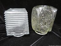 Photo showing two vintage glass lampshades, one square with horizontal ribbing and one ornate round with black paint accents.