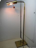 Full view of the vintage brass and metal floor reading lamp illuminated, showing its adjustable arm and shade.