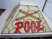 Four-sided pyramid-shaped pool table lamp shade with painted plastic design depicting crossed pool cues and billiard balls, with word 'POOL' in red letters on one side.