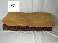 Two folded fabric pieces shown stacked: a mustard gold solid upholstery fabric on top and a heavy Victorian brocade fabric with dark red/gold floral pattern underneath.