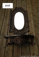 Full view of the ornate oval mirror and matching shelf mounted on wooden wall, showing overall size and design.
