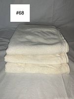 Three folded cream-colored plush towels stacked, showing texture and edges.