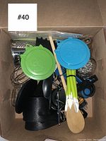 Top-down photo of a box containing kitchen utensils including rubber spatulas, whisks, graters, measuring spoons, silicone brushes, and peelers.