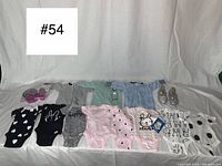 Photo shows 8 long sleeve sleepers, 3 onesies, and a pair of glitter shoes arranged neatly on a white fabric background