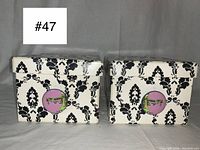 Two medium storage boxes with black and white gothic Victorian damask print and circular pin-up zombie images on the front against a light purple background, both with lids.