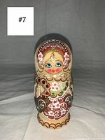 Close-up photo of one nesting doll with detailed floral and swirl hand painted patterns, blue eyes, and sparkly accents, showing vintage condition.
