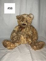 Full body image of vintage teddy bear sitting, showing curly golden fur, long limbs and overall shape