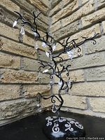 Twisted black metal tree against brick wall with hanging clear resin crystal drop ornaments attached to curved branches.