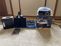 Overview of all items including projector with box, two Acoustic Research wireless speakers with center tower speaker, Sentry speaker headphones in and out of box, and Craig CD Boombox box.