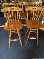 Five oak finish wooden bar stools with traditional spindle backs and turned legs, viewed from front and slightly side angle.
