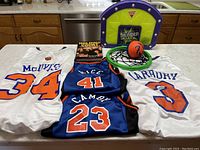 Four NY Knicks basketball jerseys, autographed book, youth basketball hoop and ball displayed on kitchen table.