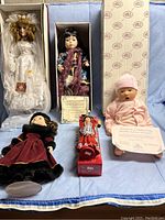 Five collectible dolls arranged on blue fabric, showing variety of styles and certificates