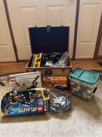 Various LEGO and magnetic building sets arranged on floor, including boxed sets, loose pieces in bags and containers, and wooden box open with parts.